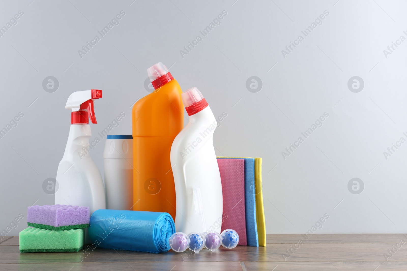 Photo of Different toilet cleaners, sponges and trash bags on wooden table against light grey background. Space for text