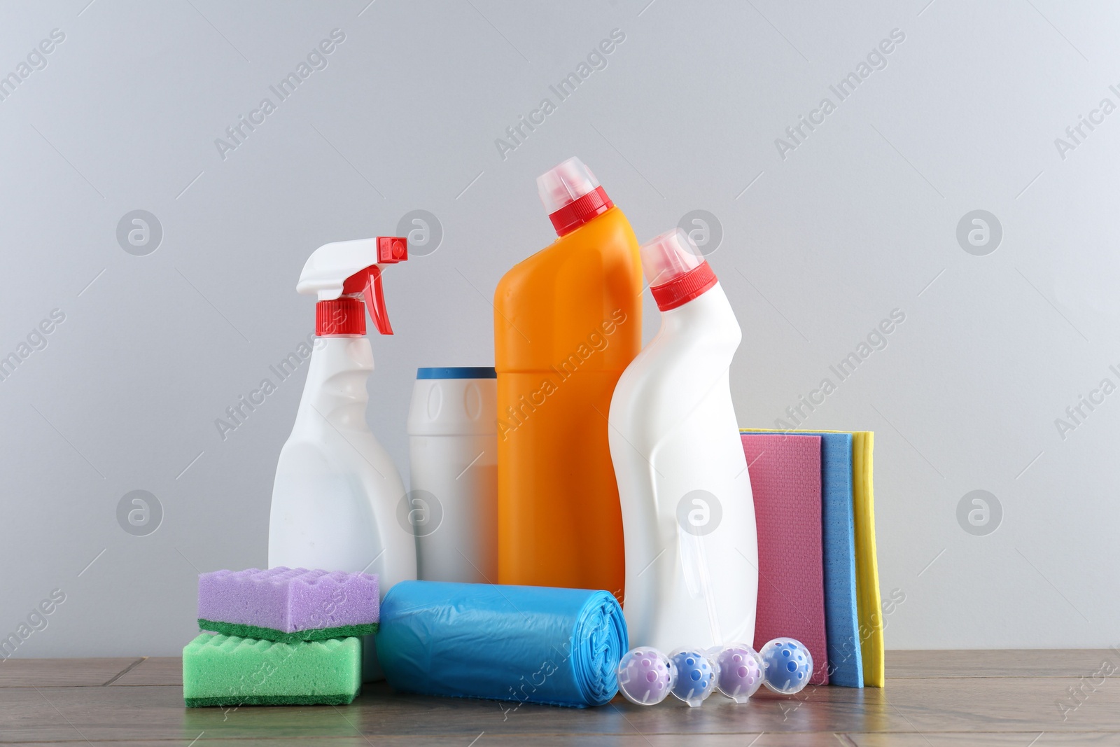 Photo of Different toilet cleaners, sponges and trash bags on wooden table against light grey background