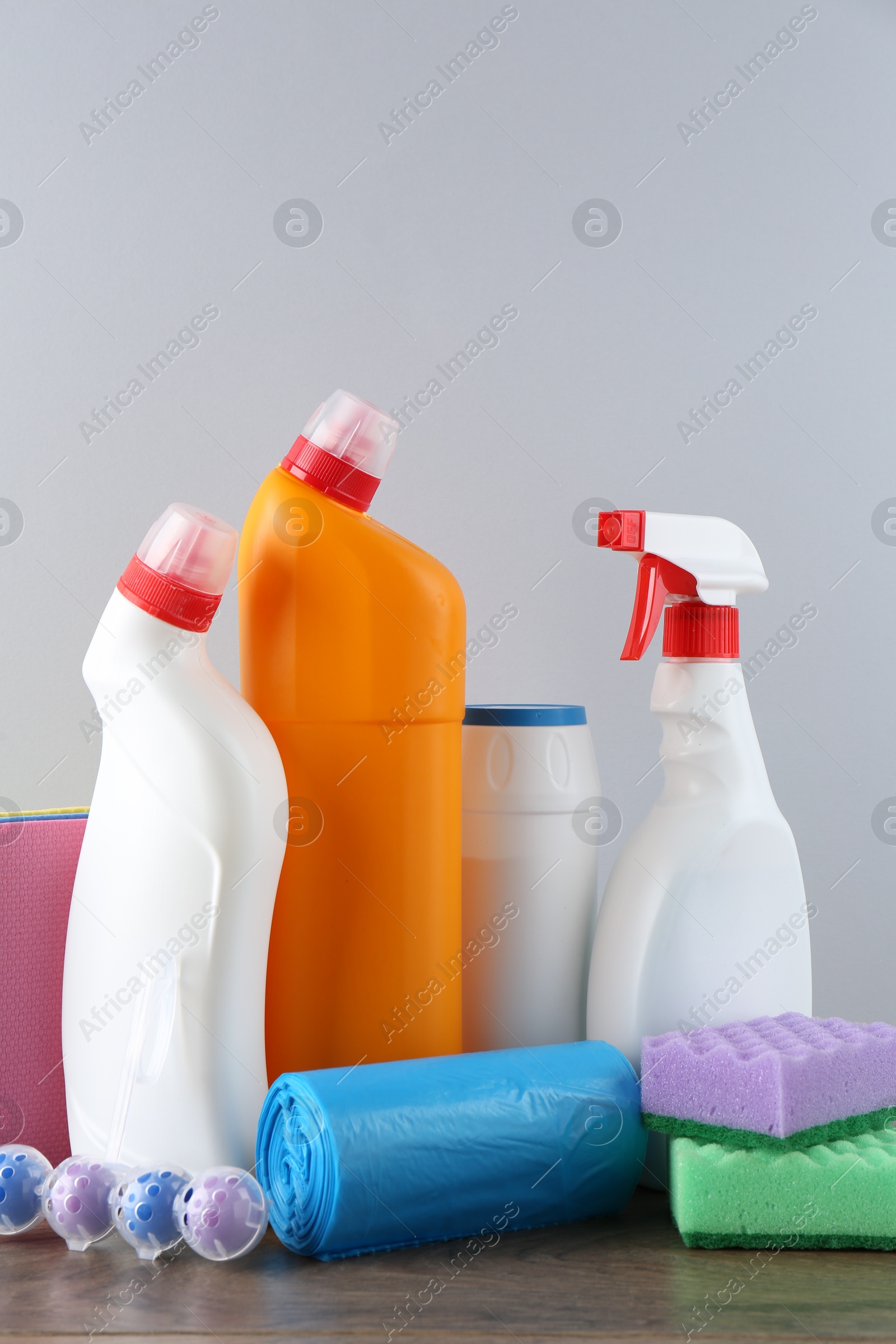 Photo of Different toilet cleaners, sponges and trash bags on wooden table against light grey background