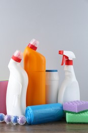 Photo of Different toilet cleaners, sponges and trash bags on wooden table against light grey background