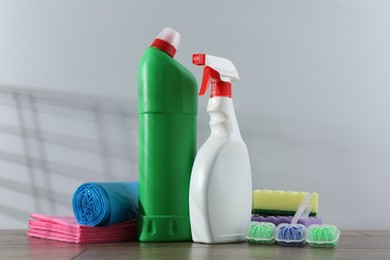 Photo of Different toilet cleaners, sponges and trash bags on wooden table against light grey background