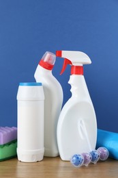 Photo of Different toilet cleaners, sponges and trash bags on wooden table against blue background