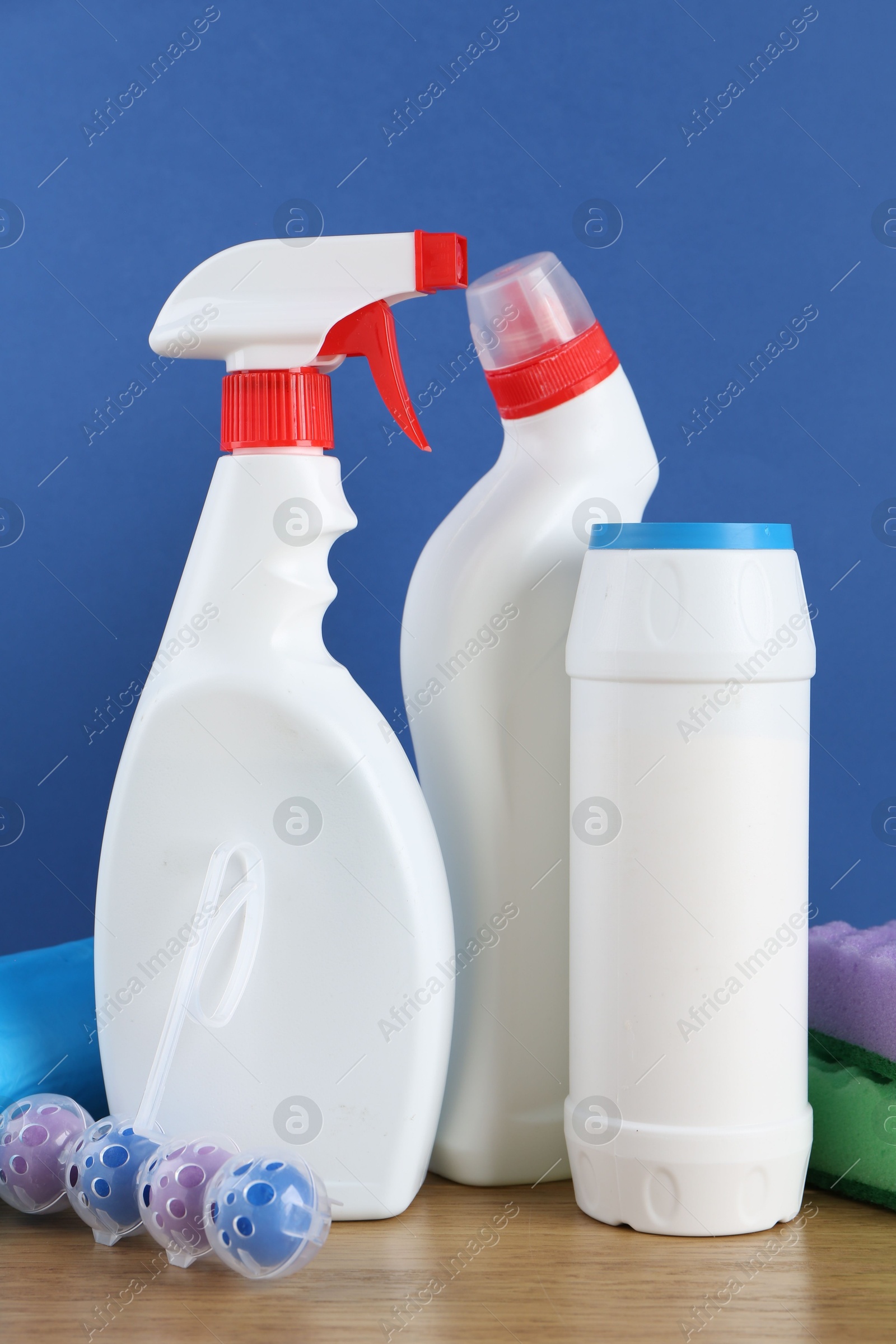 Photo of Different toilet cleaners, sponges and trash bags on wooden table against blue background