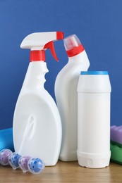 Photo of Different toilet cleaners, sponges and trash bags on wooden table against blue background