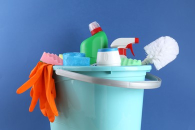 Photo of Bucket with different toilet cleaners, sponges, rubber gloves and trash bags on blue background