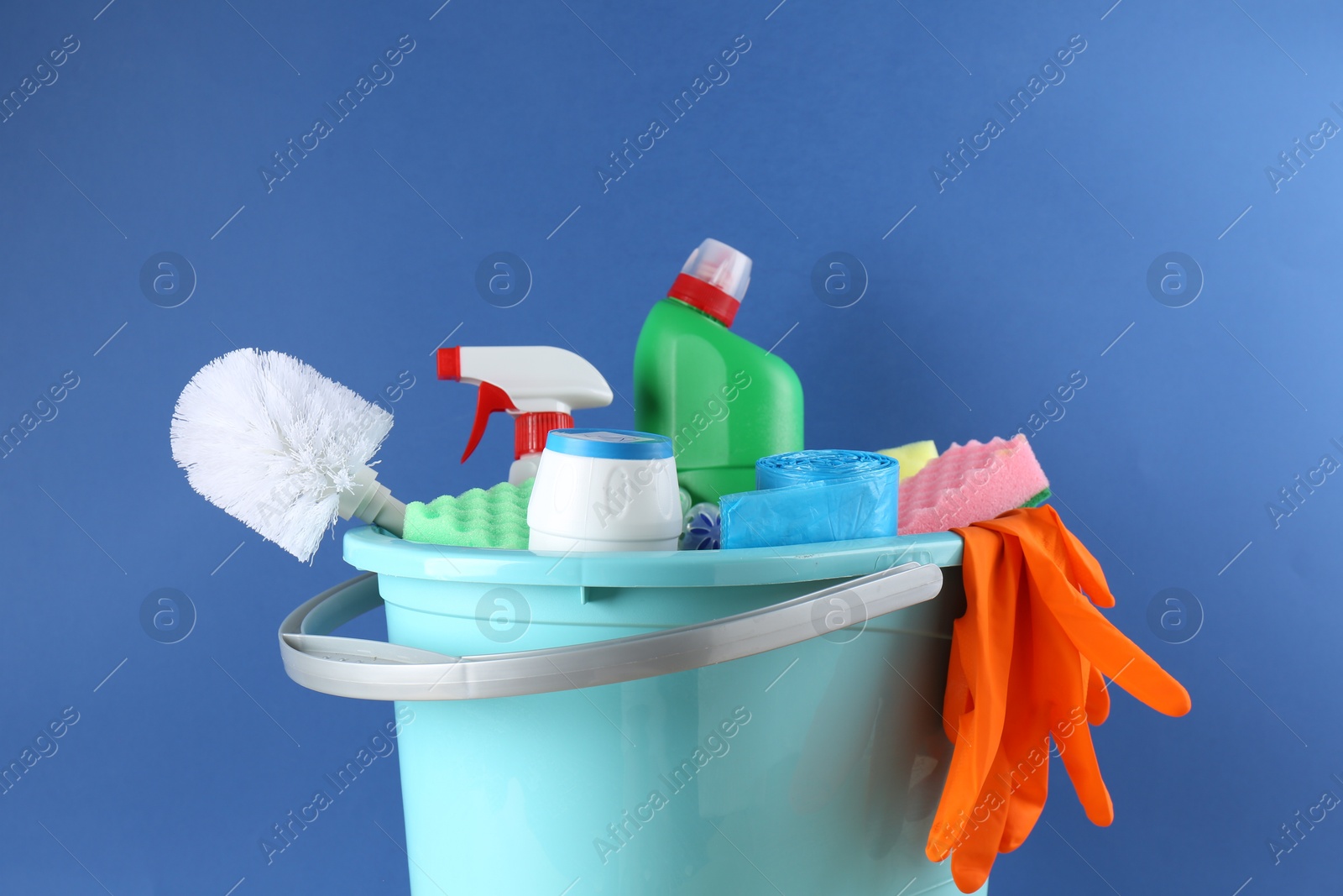 Photo of Bucket with different toilet cleaners, sponges, rubber gloves and trash bags on blue background