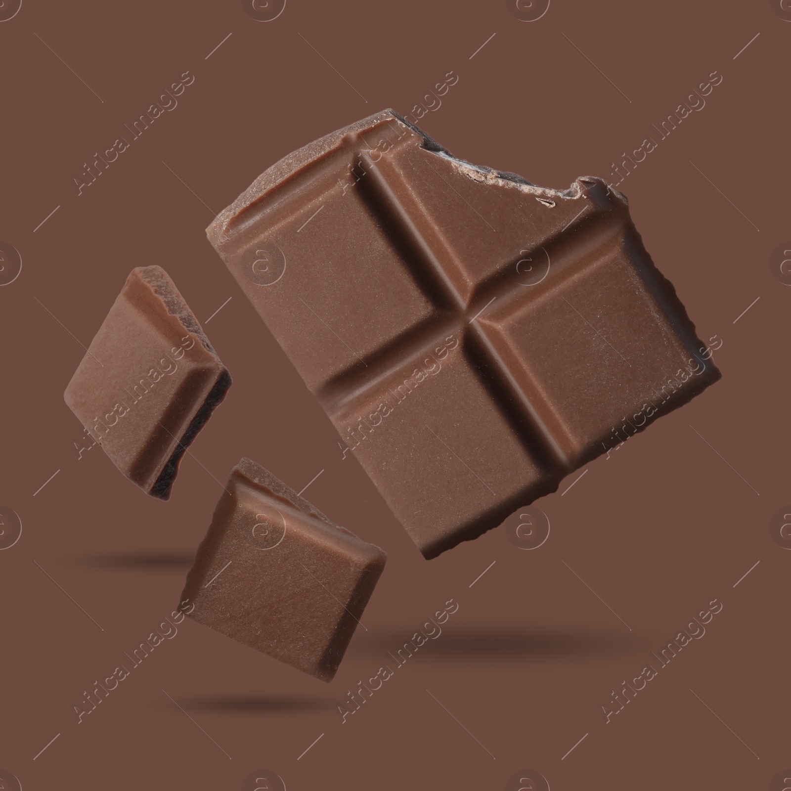 Image of Pieces of sweet chocolate falling on brown background