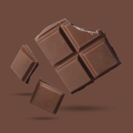 Image of Pieces of sweet chocolate falling on brown background