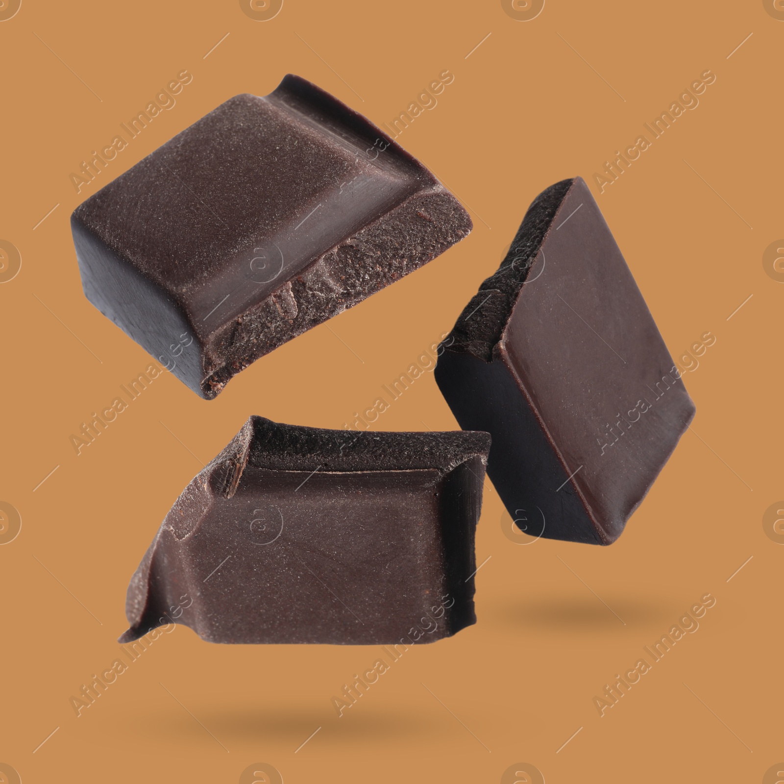 Image of Pieces of sweet chocolate falling on dark orange background