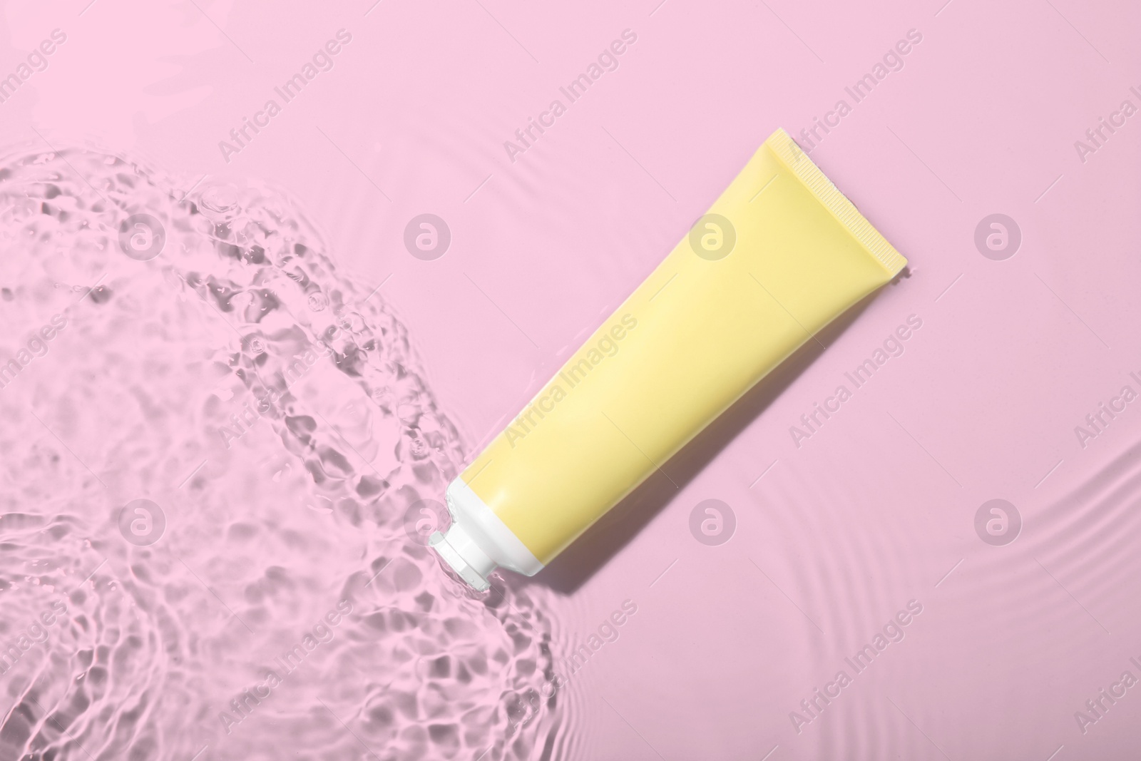 Photo of Cosmetic product. Tube with cream in water on light background, top view