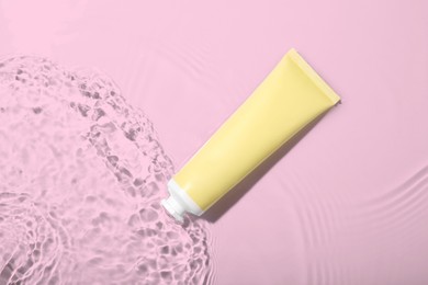 Photo of Cosmetic product. Tube with cream in water on light background, top view