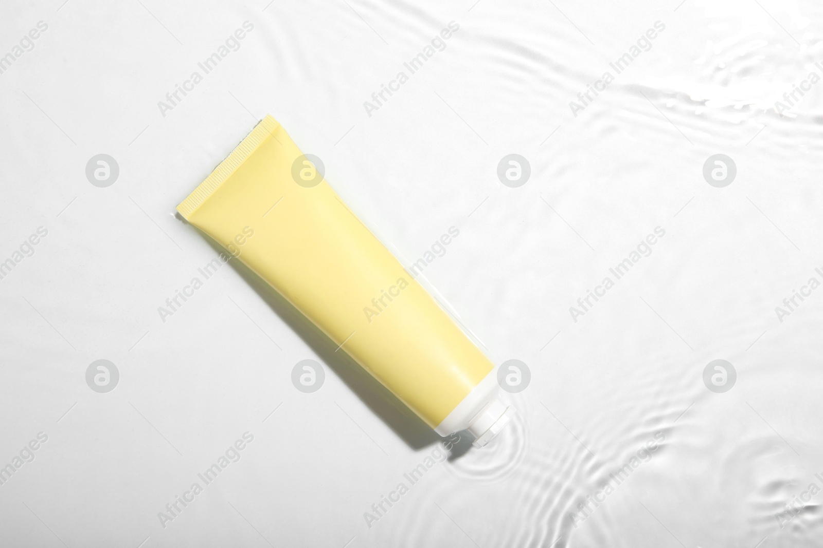 Photo of Cosmetic product. Tube with cream in water on light background, top view