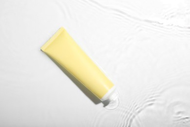 Photo of Cosmetic product. Tube with cream in water on light background, top view