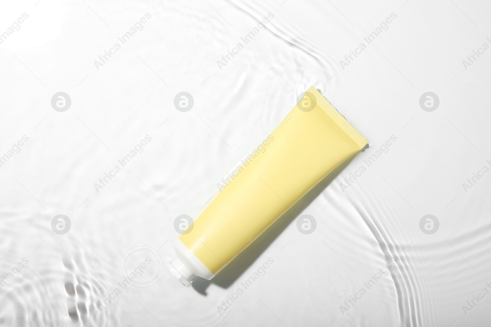 Photo of Cosmetic product. Tube with cream in water on light background, top view