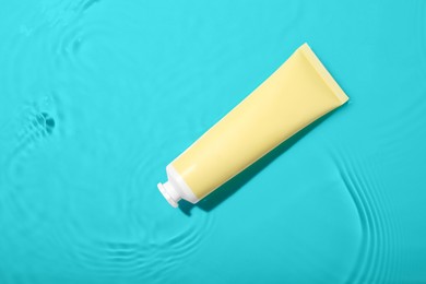 Photo of Cosmetic product. Tube with cream in water on light background, top view