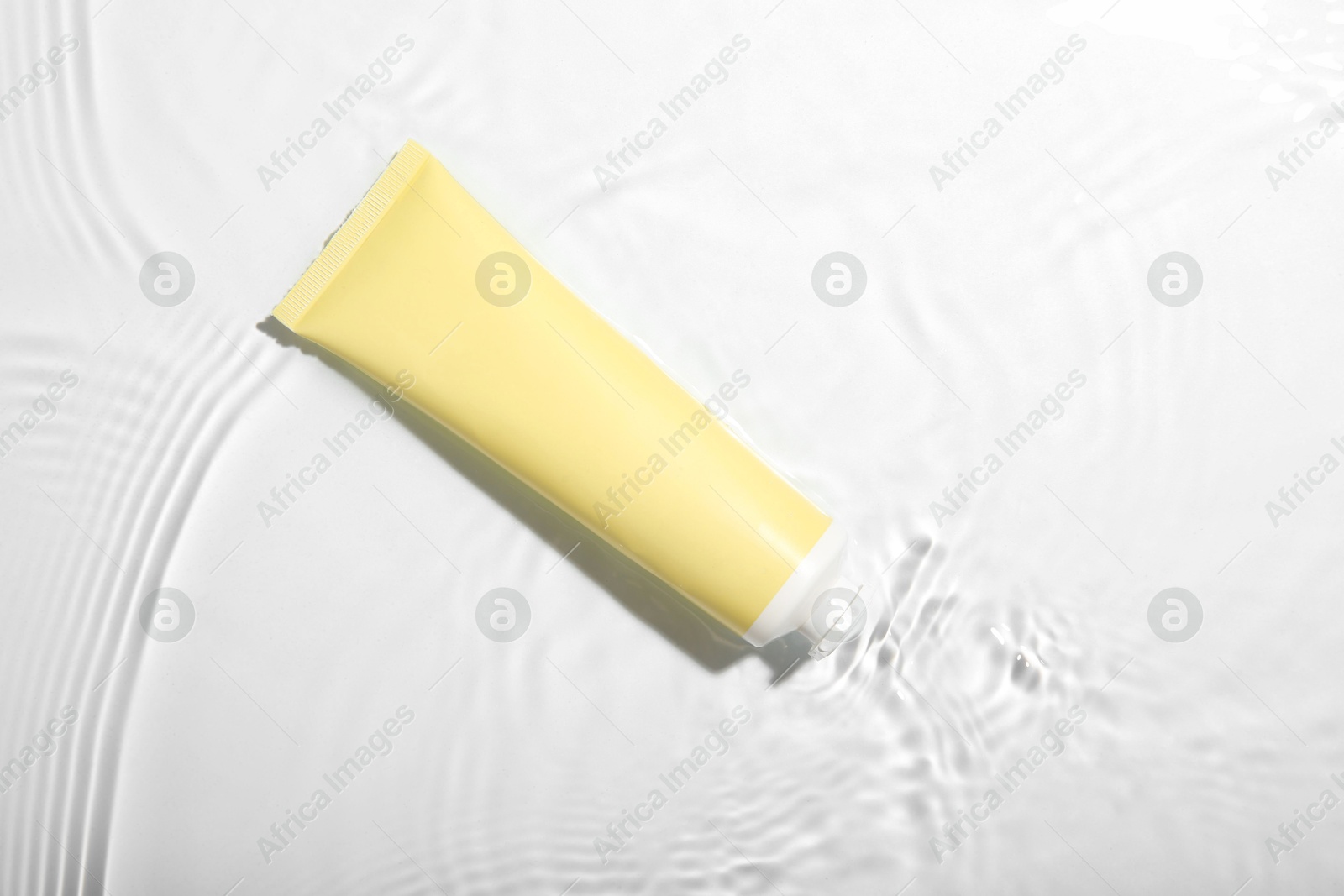 Photo of Cosmetic product. Tube with cream in water on light background, top view