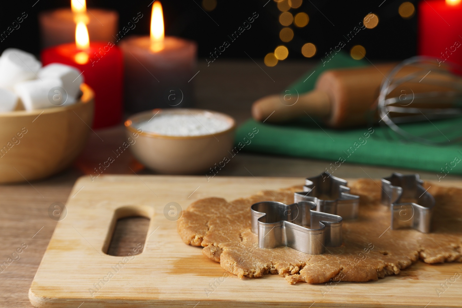 Photo of Raw dough, cookie cutters, flour, marshmallows, kitchen tools and burning candles on wooden table