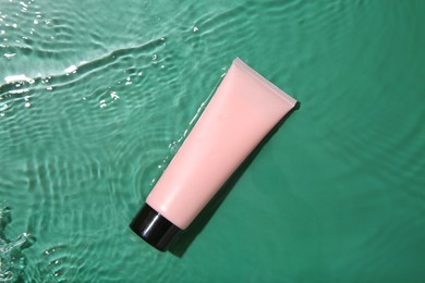 Photo of Cosmetic product. Tube with cream in water on green background, top view