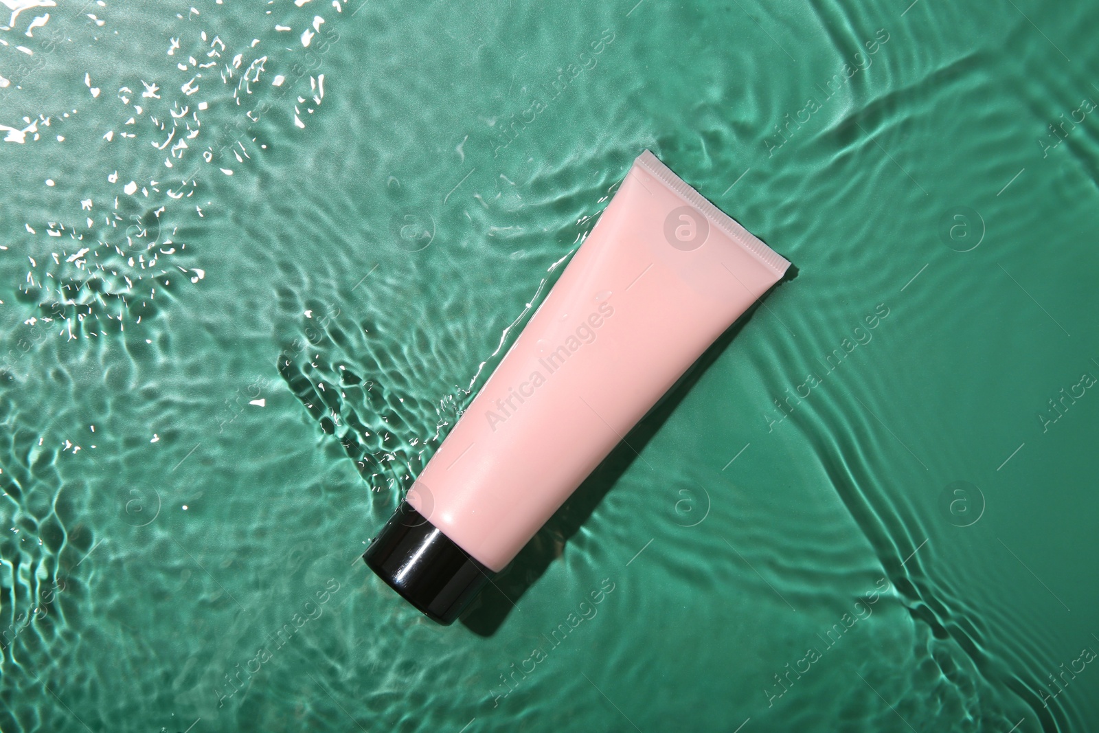 Photo of Cosmetic product. Tube with cream in water on green background, top view