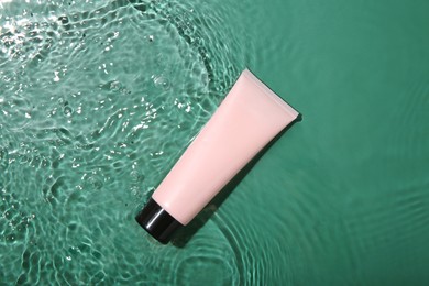 Cosmetic product. Tube with cream in water on green background, top view