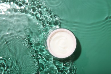 Photo of Cosmetic product. Jar with cream in water on green background, top view