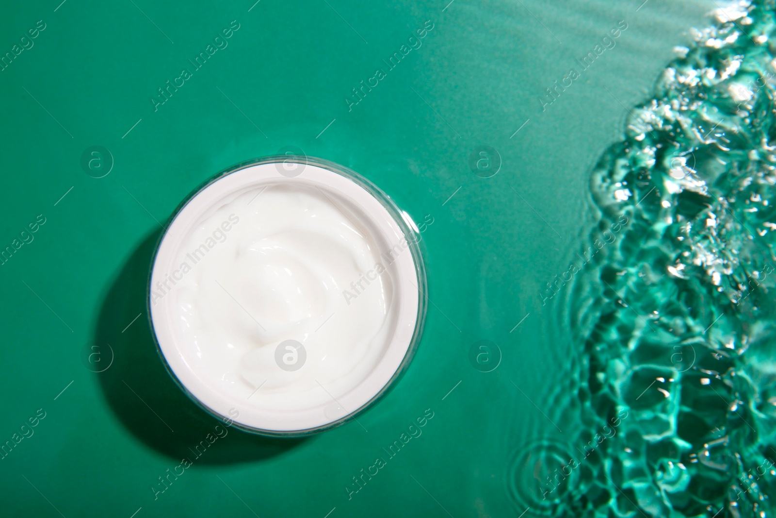 Photo of Cosmetic product. Jar with cream in water on green background, top view. Space for text