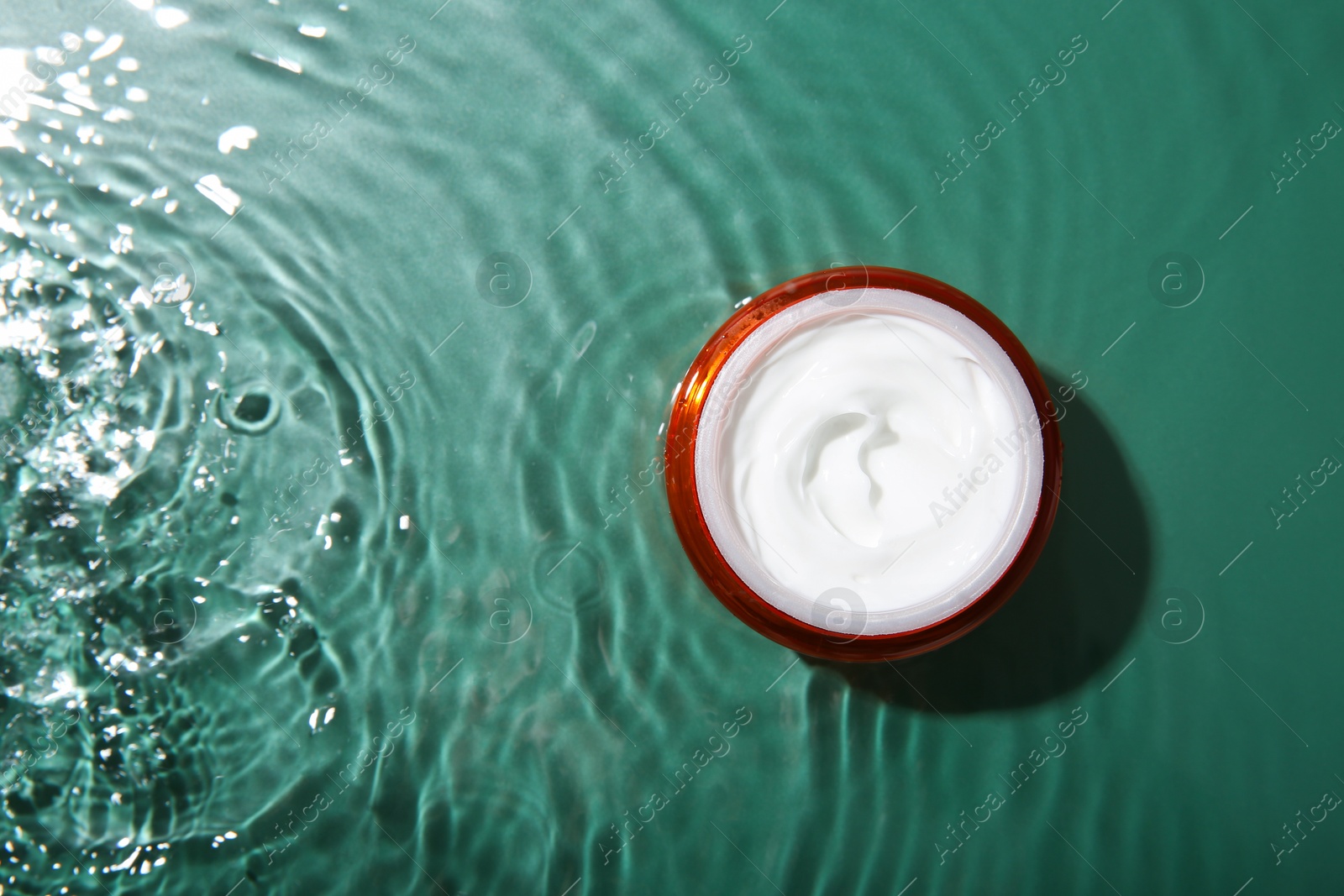 Photo of Cosmetic product. Jar with cream in water on green background, top view. Space for text