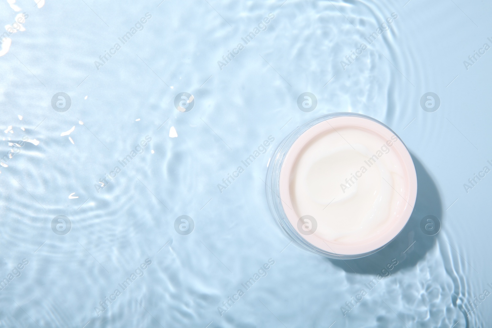 Photo of Cosmetic product. Jar with cream in water on light blue background, top view. Space for text