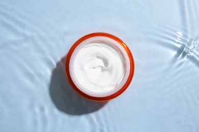 Photo of Cosmetic product. Jar with cream in water on light blue background, top view