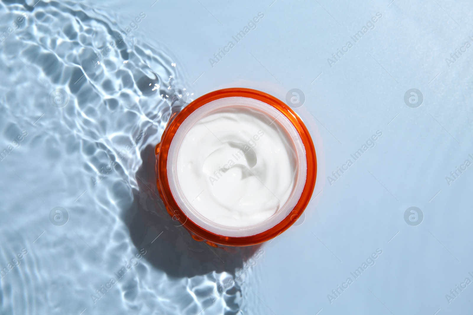 Photo of Cosmetic product. Jar with cream in water on light blue background, top view