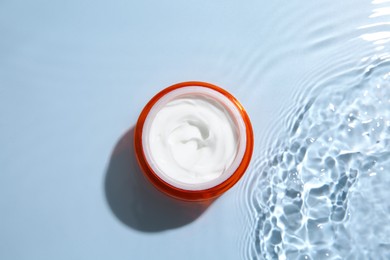 Photo of Cosmetic product. Jar with cream in water on light blue background, top view