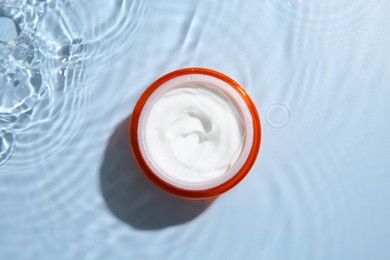 Cosmetic product. Jar with cream in water on light blue background, top view