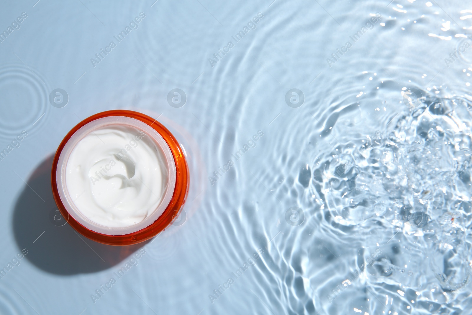 Photo of Cosmetic product. Jar with cream in water on light blue background, top view. Space for text