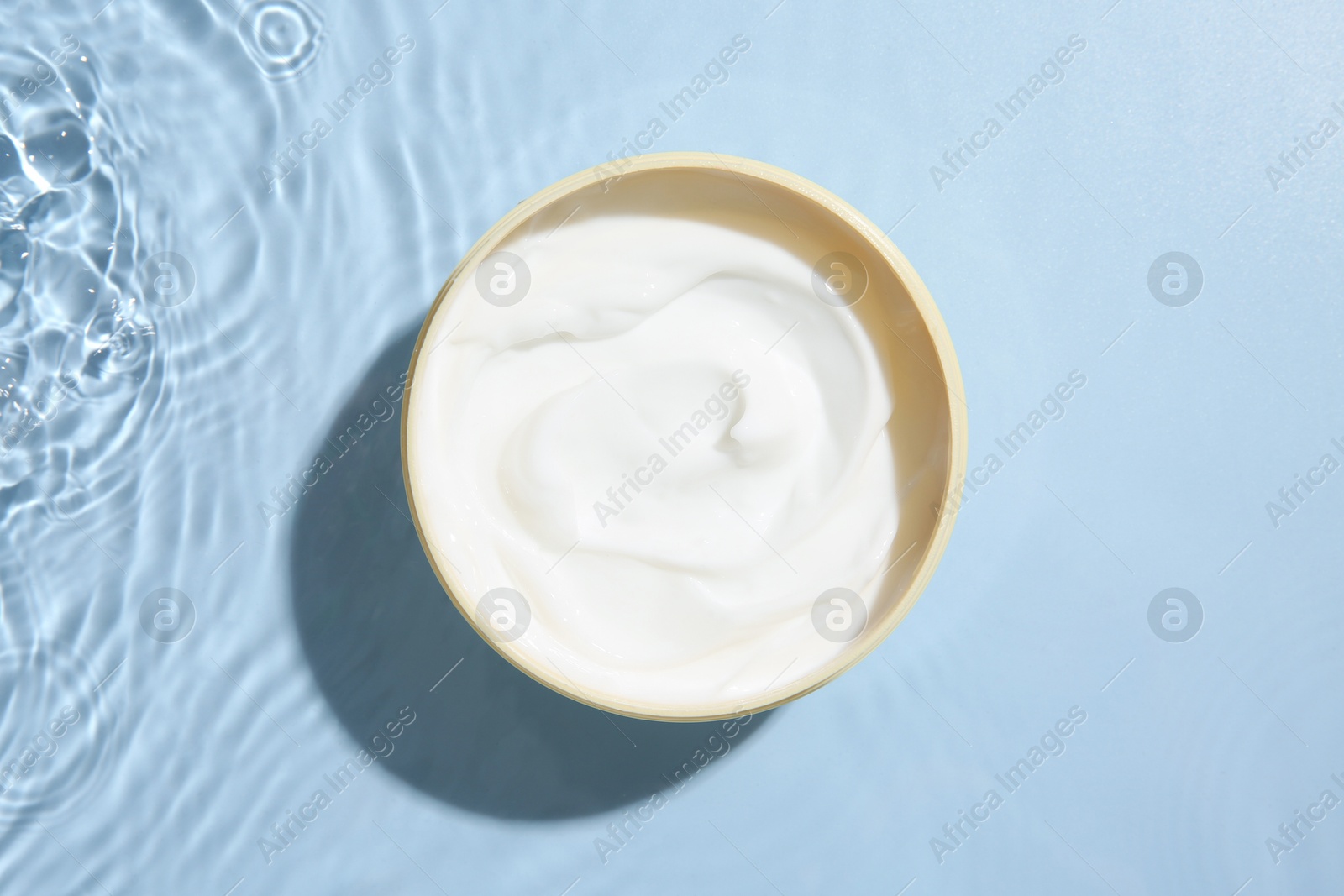 Photo of Cosmetic product. Jar with cream in water on light blue background, top view