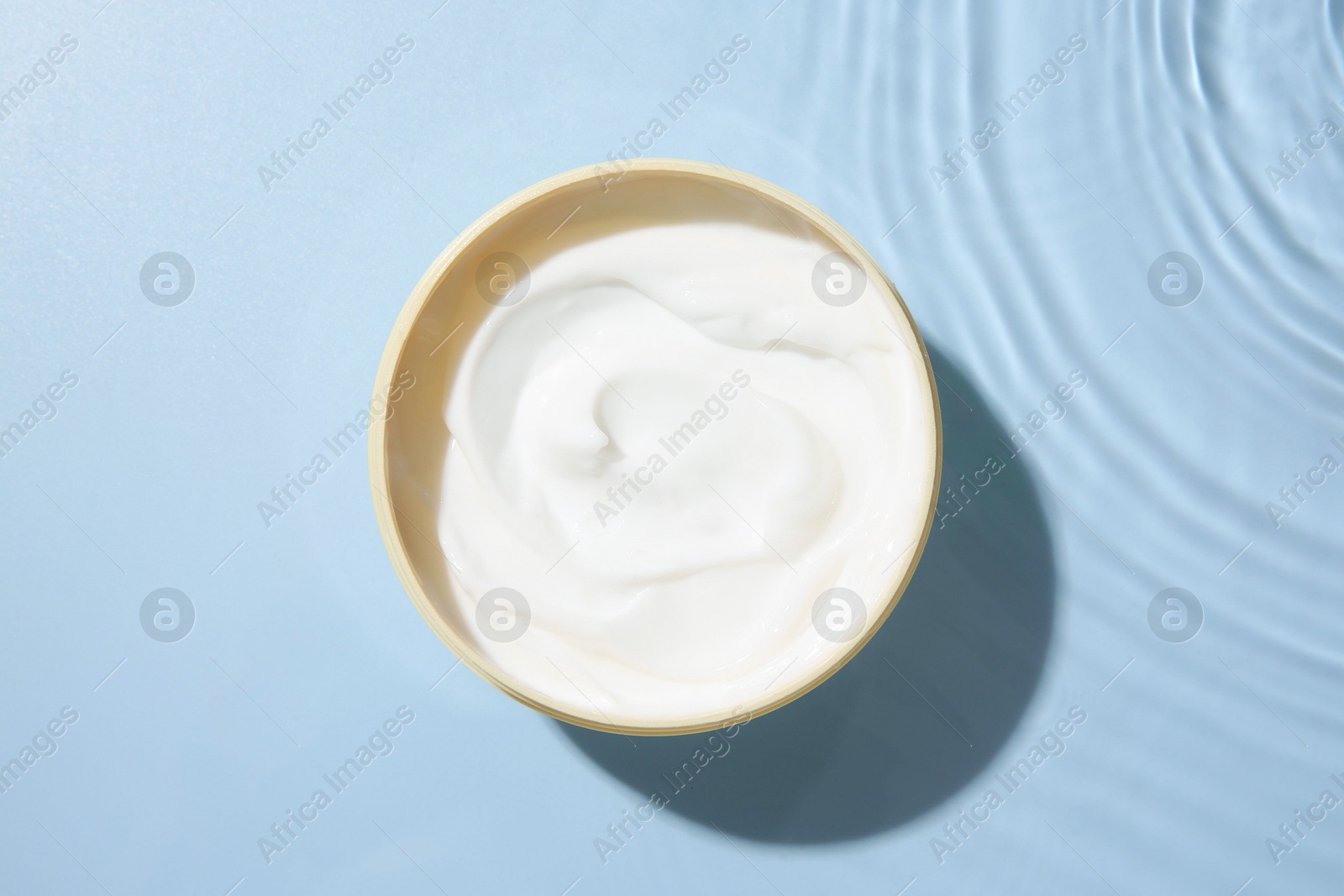 Photo of Cosmetic product. Jar with cream in water on light blue background, top view