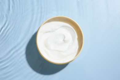 Cosmetic product. Jar with cream in water on light blue background, top view