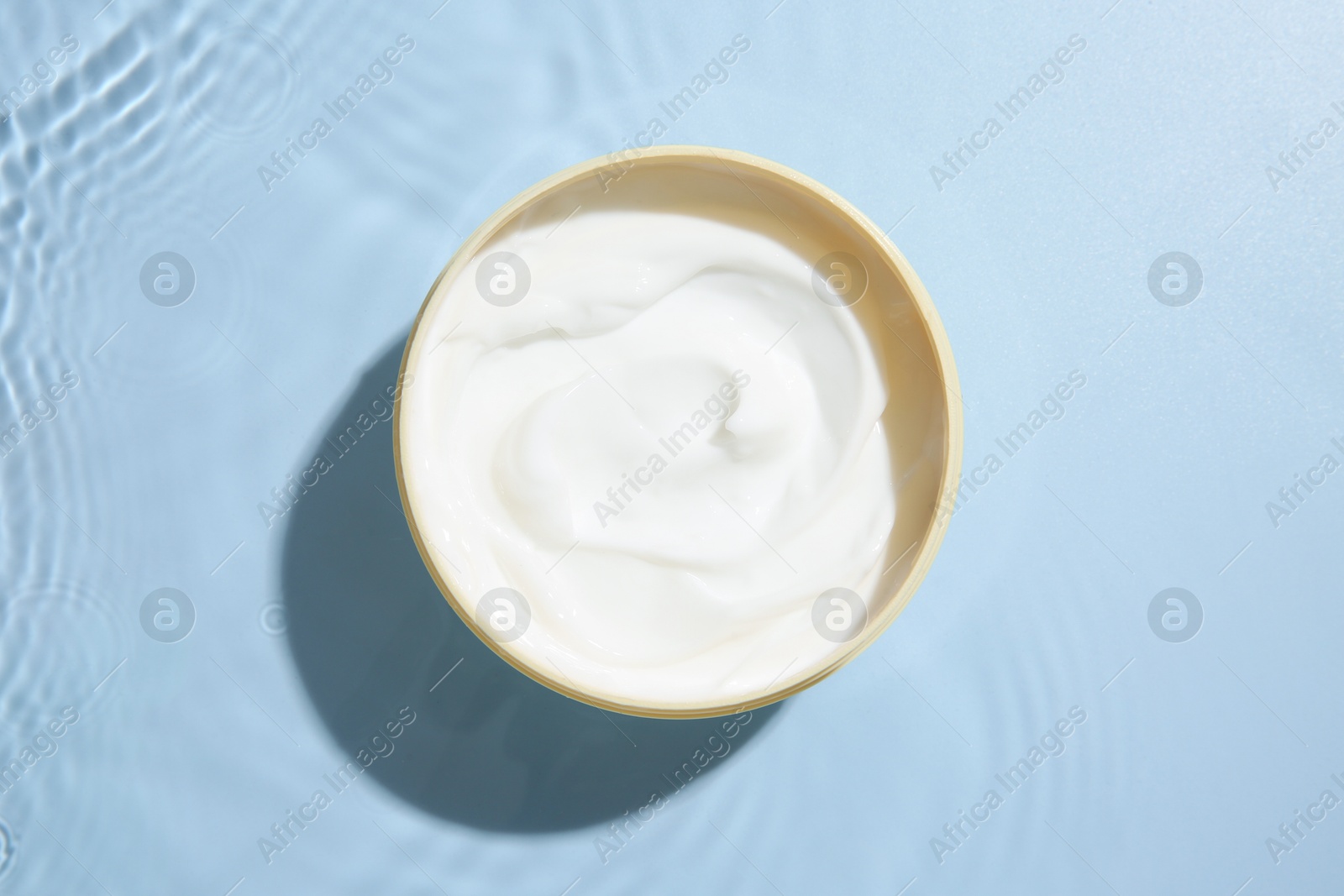 Photo of Cosmetic product. Jar with cream in water on light blue background, top view