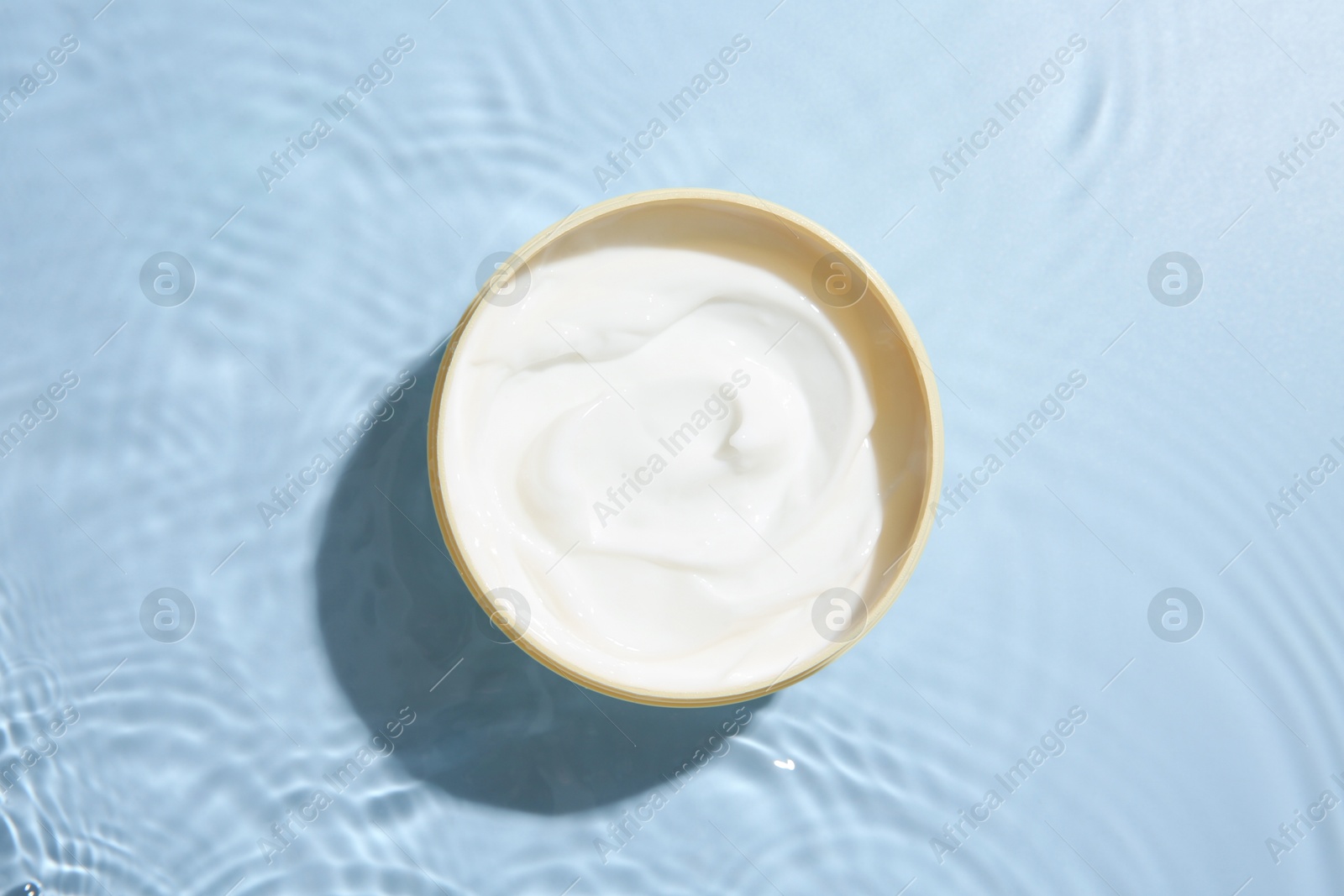 Photo of Cosmetic product. Jar with cream in water on light blue background, top view