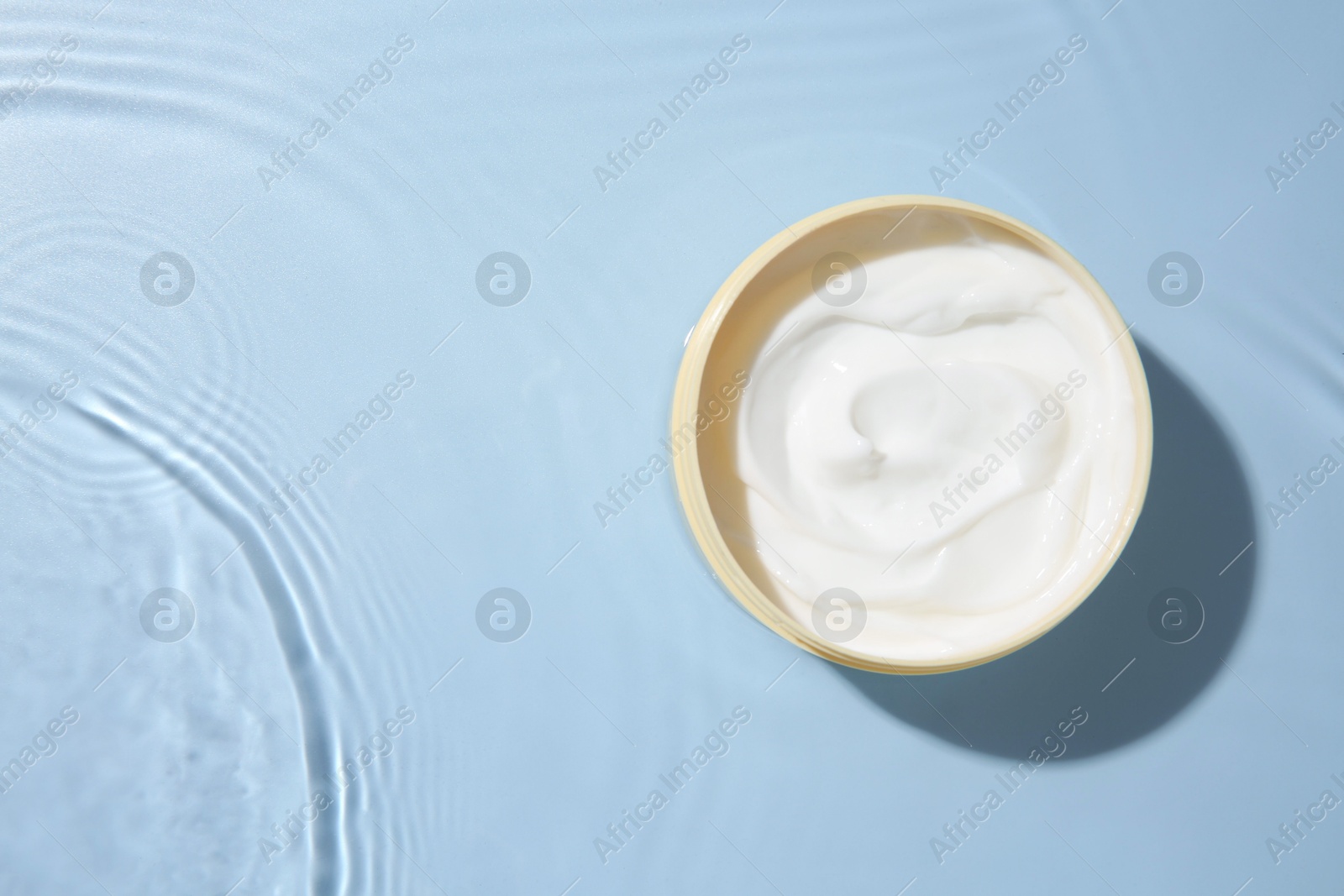 Photo of Cosmetic product. Jar with cream in water on light blue background, top view. Space for text