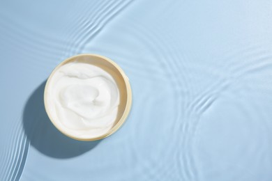 Photo of Cosmetic product. Jar with cream in water on light blue background, top view. Space for text