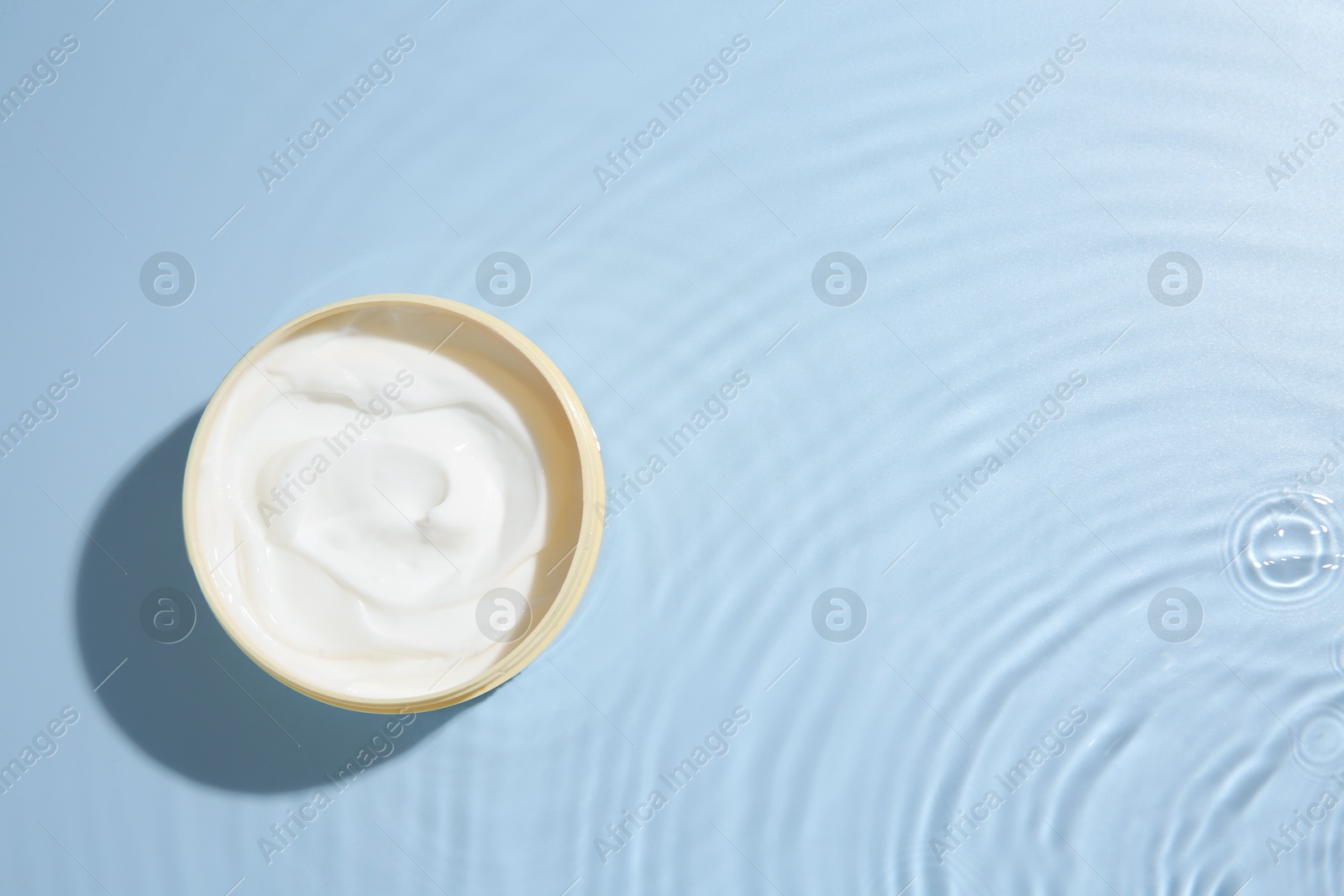 Photo of Cosmetic product. Jar with cream in water on light blue background, top view. Space for text