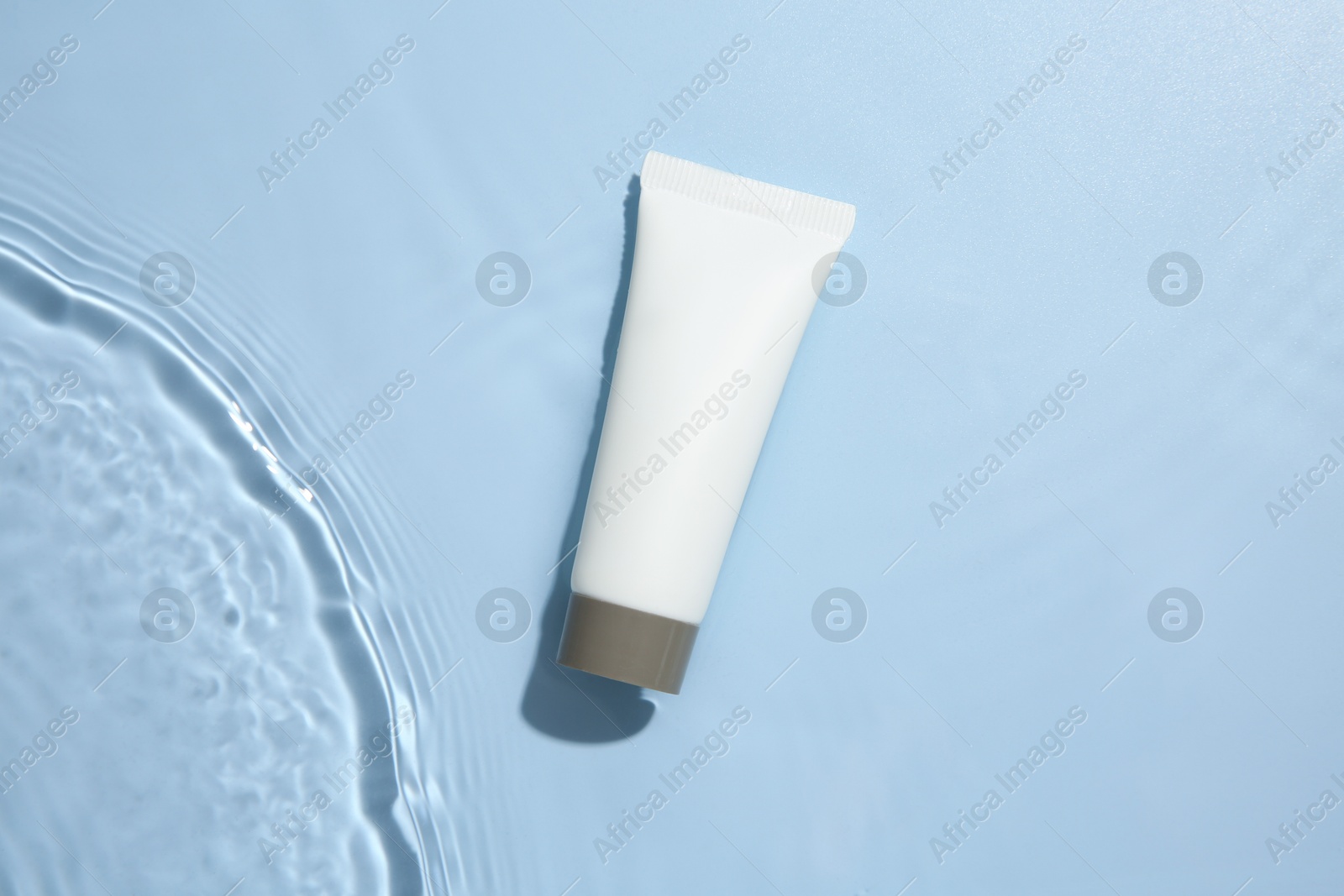 Photo of Cosmetic product. Tube with cream in water on light blue background, top view