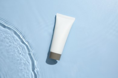 Cosmetic product. Tube with cream in water on light blue background, top view