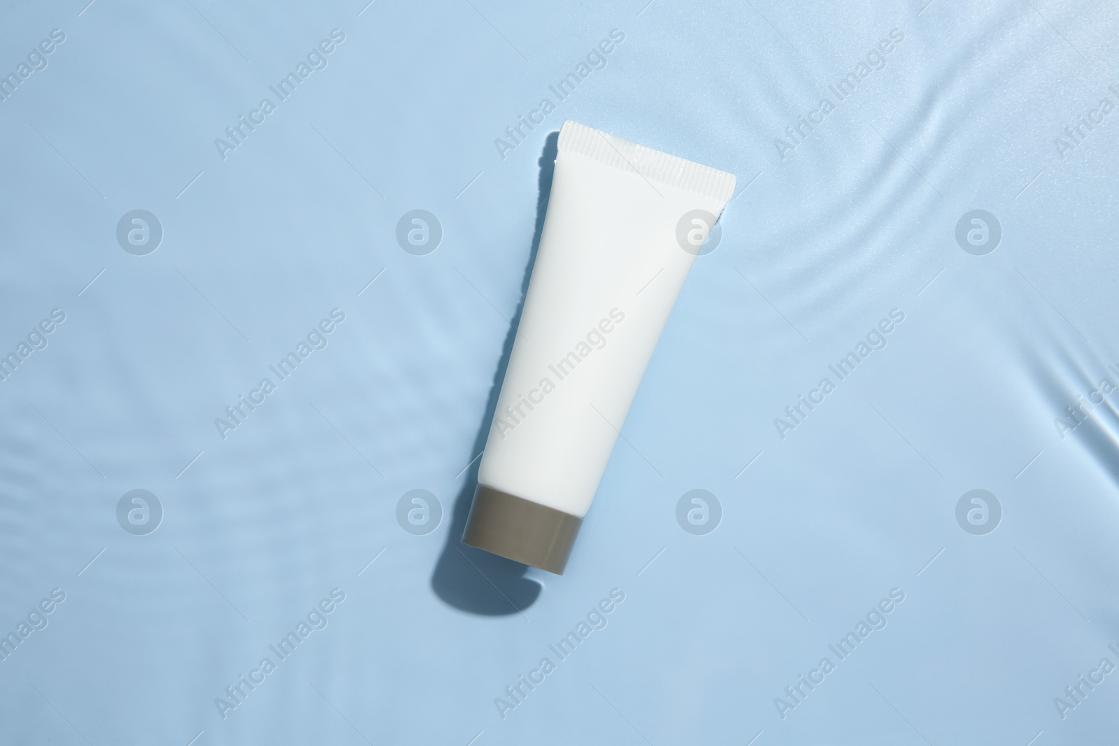 Photo of Cosmetic product. Tube with cream in water on light blue background, top view