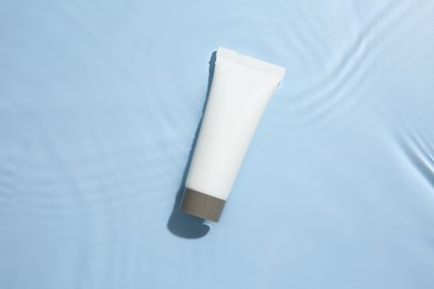 Photo of Cosmetic product. Tube with cream in water on light blue background, top view