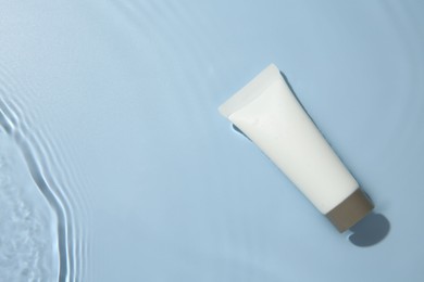 Photo of Cosmetic product. Tube with cream in water on light blue background, top view. Space for text