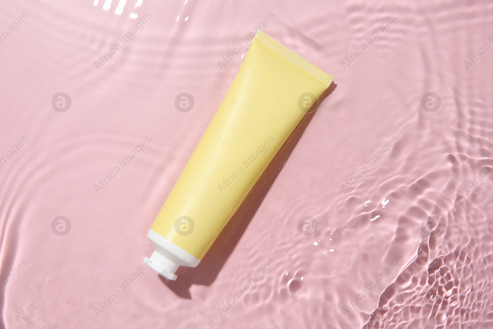 Photo of Cosmetic product. Tube with cream in water on pink background, top view