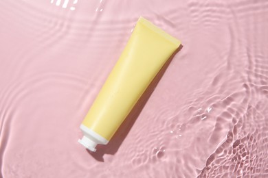 Cosmetic product. Tube with cream in water on pink background, top view