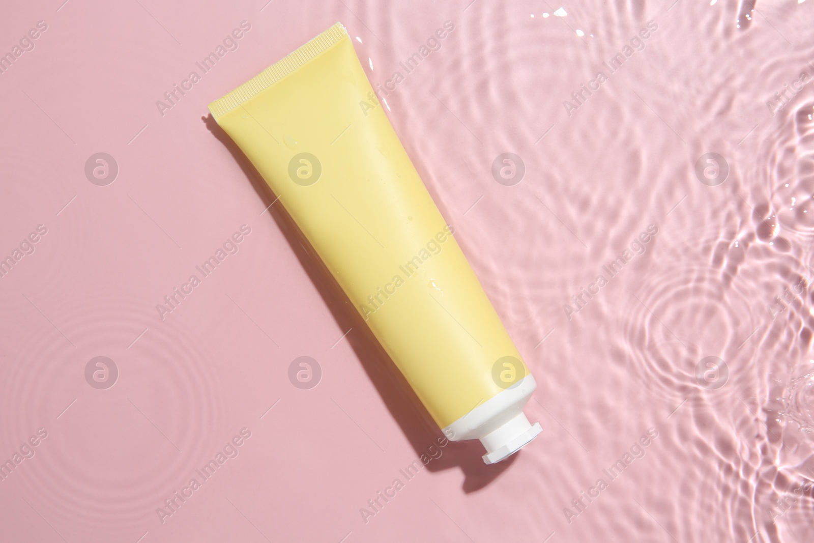 Photo of Cosmetic product. Tube with cream in water on pink background, top view