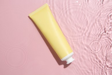 Cosmetic product. Tube with cream in water on pink background, top view